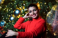 a woman posing in front of a christmas tree