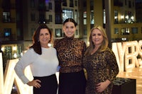 three women posing for a photo in front of a sign