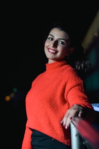 a woman in a red sweater leaning on a railing at night